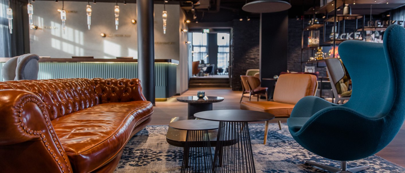 Moderne Hotellobby mit braunem Ledersofa, blauem Sessel, Couchtischen und stilvoller Beleuchtung. Elegantes, gemütliches Ambiente., © TOMAS Moderne Hotellobby mit braunem Ledersofa, blauem Sessel, Couchtischen und stilvoller Beleuchtung. Elegantes, gemütliches Ambiente., © TOMAS