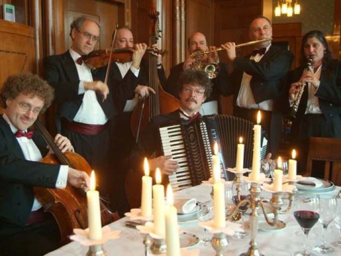 Musiker in Abendgarderobe spielen Instrumente um einen festlich gedeckten Tisch mit Kerzen., © Stadt Murrhardt Musiker in Abendgarderobe spielen Instrumente um einen festlich gedeckten Tisch mit Kerzen., © Stadt Murrhardt