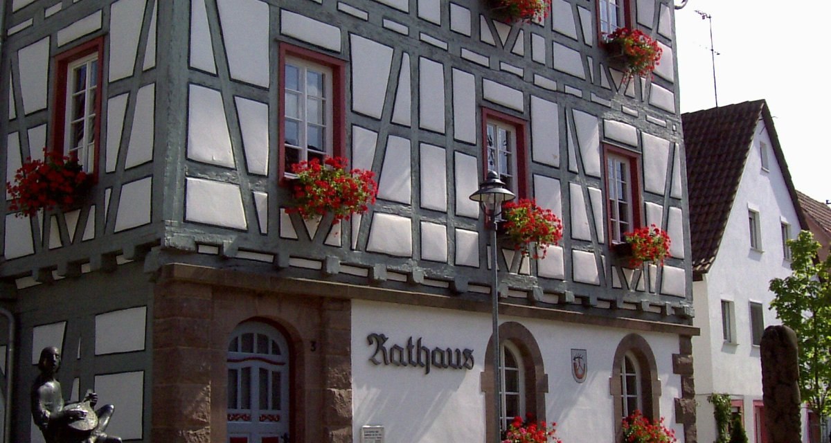 Fachwerk-Rathaus mit roten Blumen an den Fenstern. Eine Statue steht vor dem Gebäude auf einem gepflasterten Platz., © Land der 1000 Hügel - Kraichgau-Stromberg Fachwerk-Rathaus mit roten Blumen an den Fenstern. Eine Statue steht vor dem Gebäude auf einem gepflasterten Platz., © Land der 1000 Hügel - Kraichgau-Stromberg