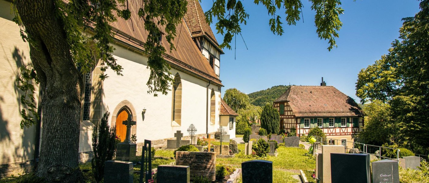 Die Walterichskirche in Murrhardt mit ihrem Friedhof und einem Fachwerkhaus im Hintergrund an einem sonnigen Tag., © Stuttgart-Marketing GmbH, Sarah Schmid Die Walterichskirche in Murrhardt mit ihrem Friedhof und einem Fachwerkhaus im Hintergrund an einem sonnigen Tag., © Stuttgart-Marketing GmbH, Sarah Schmid