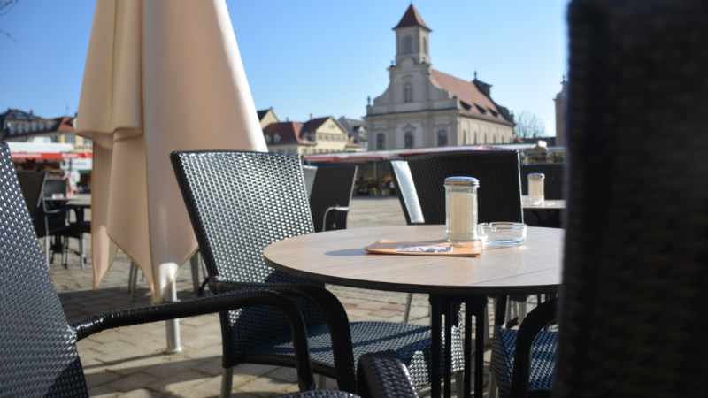 Leerer Außenbereich eines Cafés mit Tischen und Stühlen, im Hintergrund eine Kirche bei klarem Himmel., © Konditorei Lutz Leerer Außenbereich eines Cafés mit Tischen und Stühlen, im Hintergrund eine Kirche bei klarem Himmel., © Konditorei Lutz