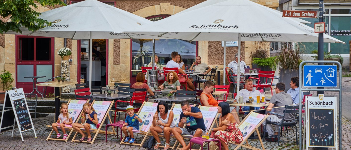 Menschen sitzen unter Sonnenschirmen vor dem FRIEDRICH Café in Waldenbuch. Kinder und Erwachsene entspannen auf Stühlen und Liegestühlen., © thomas ceska waldenbuch