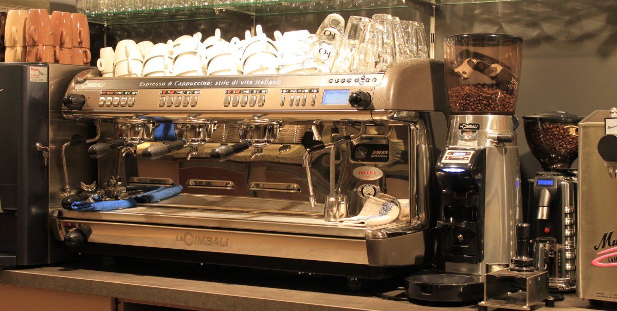 Eine professionelle Espressomaschine von La Cimbali mit Tassen und Gläsern auf einem Regal in einem Café.