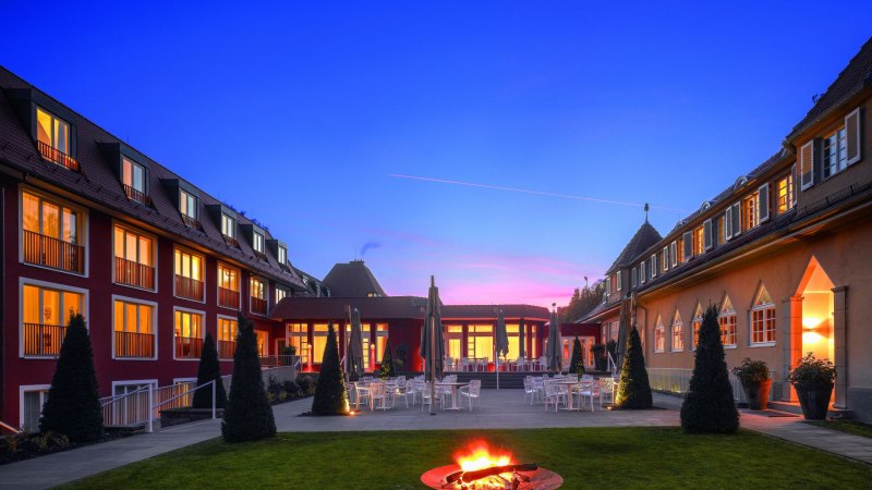 Das Waldhotel Stuttgart bei D&auml;mmerung, mit beleuchteten Fenstern und einer Feuerstelle im Garten. Der Himmel ist blau mit einem rosa Streifen., &copy; Waldhotel Stuttgart GmbH