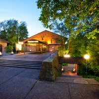 Eingang des Perkins Park in Stuttgart bei Dämmerung, umgeben von Bäumen und beleuchtet mit Laternen., © PerkinsPark