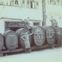 Männer posieren vor großen Holzfässern mit der Aufschrift 'Gust. Maurer'. Personen schauen aus den Fenstern eines Gebäudes., © Stadt Leonberg