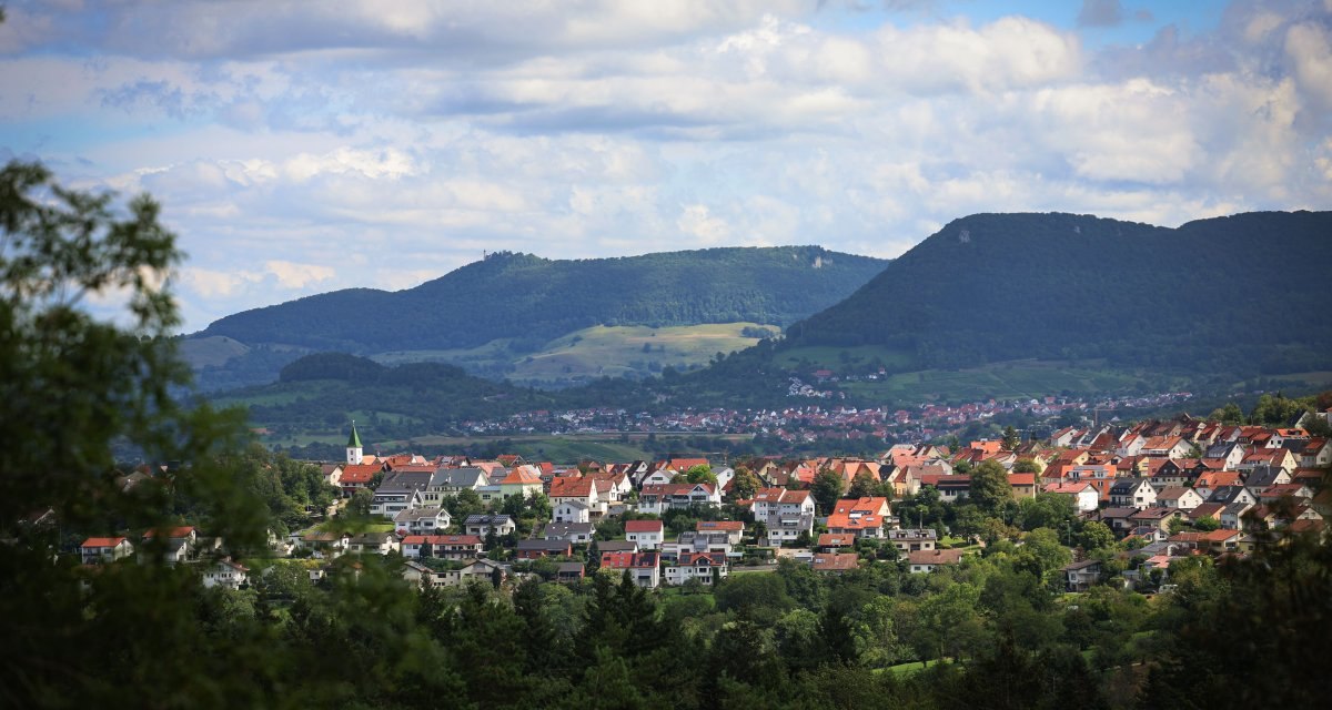 Kleine Stadt mit roten Dächern, umgeben von grünen Hügeln und Wäldern. Bewölkter Himmel im Hintergrund. Kleine Stadt mit roten Dächern, umgeben von grünen Hügeln und Wäldern. Bewölkter Himmel im Hintergrund.