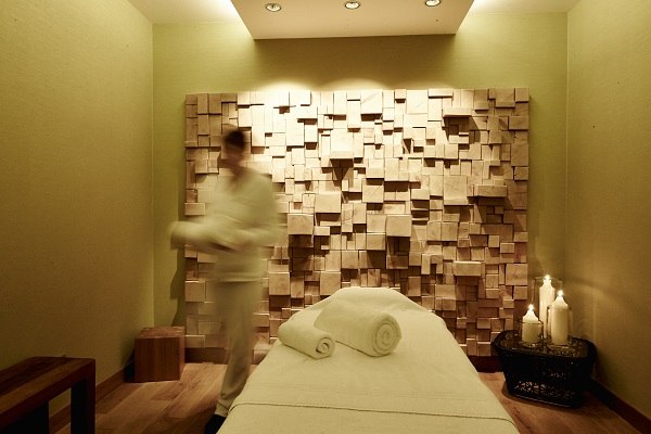 Ein Massageraum mit Holzdekorwand, Massageliege und Kerzen im Waldhotel Stuttgart. Eine Person bewegt sich im Raum., © Waldhotel Stuttgart GmbH Ein Massageraum mit Holzdekorwand, Massageliege und Kerzen im Waldhotel Stuttgart. Eine Person bewegt sich im Raum., © Waldhotel Stuttgart GmbH