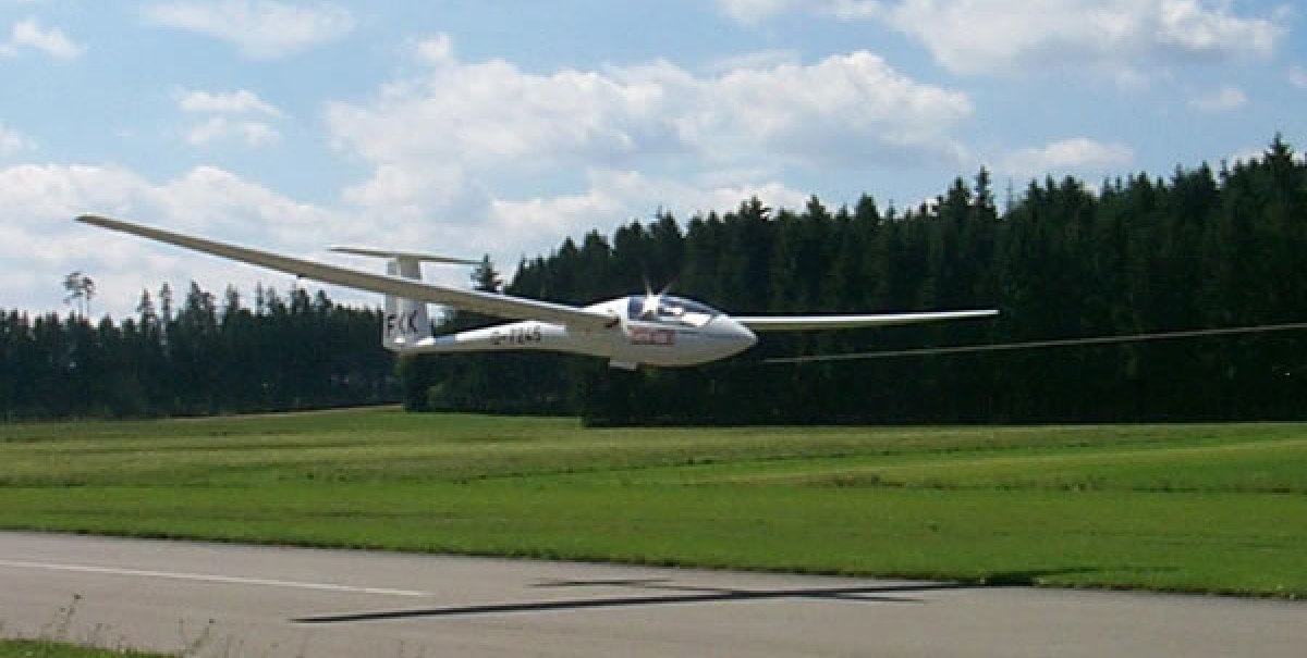 Segelflugzeug im Landeanflug auf asphaltierte Landebahn, umgeben von Wiesen und Wald. Der Himmel ist leicht bewölkt., © Aero-Club Esslingen e.V.