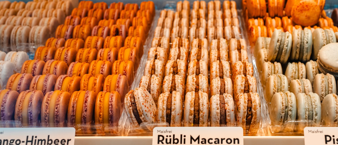 Macarons in verschiedenen Geschmacksrichtungen wie Vanille, Rübli und Aperol-Orange in einer Auslage präsentiert., © SMG, Sarah Schmid Macarons in verschiedenen Geschmacksrichtungen wie Vanille, Rübli und Aperol-Orange in einer Auslage präsentiert., © SMG, Sarah Schmid