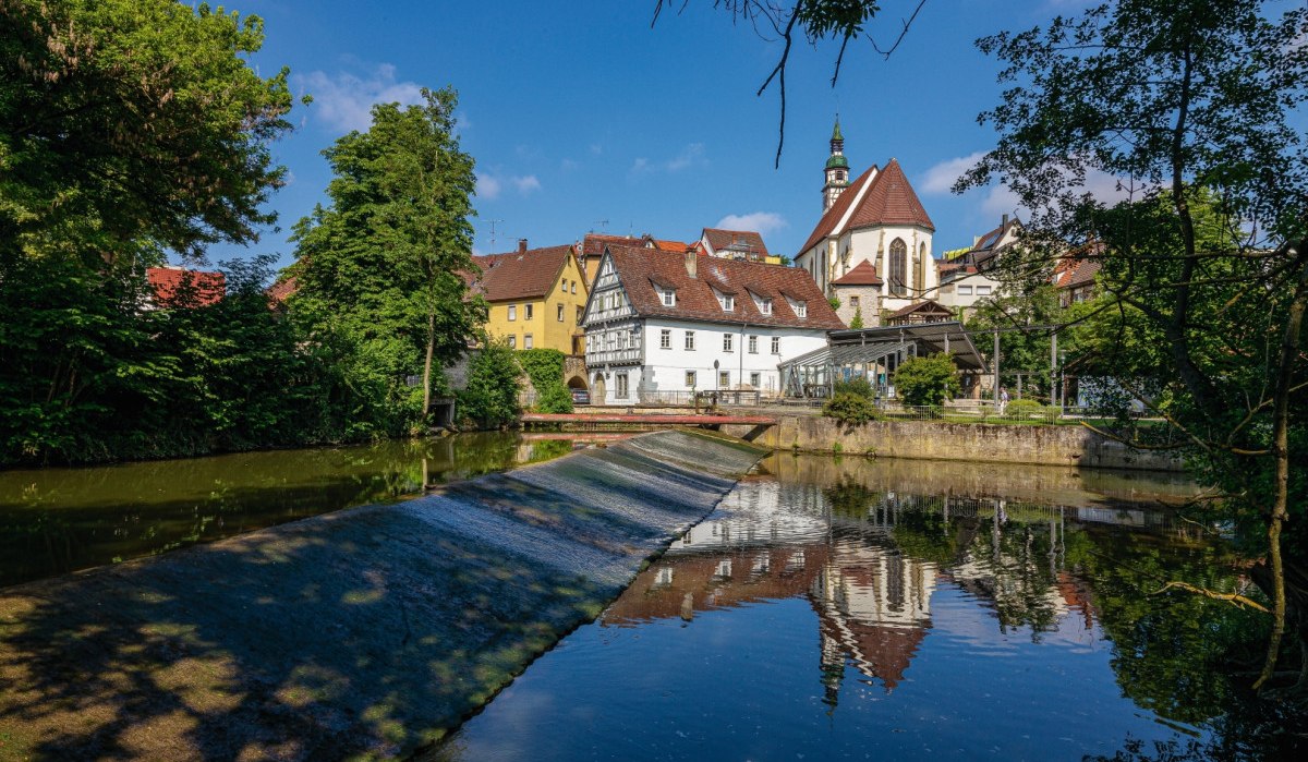 Die Rems in Waiblingen mit Fachwerkhäusern und einer Kirche im Hintergrund, umgeben von Bäumen und blauem Himmel., © Remstal Tourismus e.V. Die Rems in Waiblingen mit Fachwerkhäusern und einer Kirche im Hintergrund, umgeben von Bäumen und blauem Himmel., © Remstal Tourismus e.V.