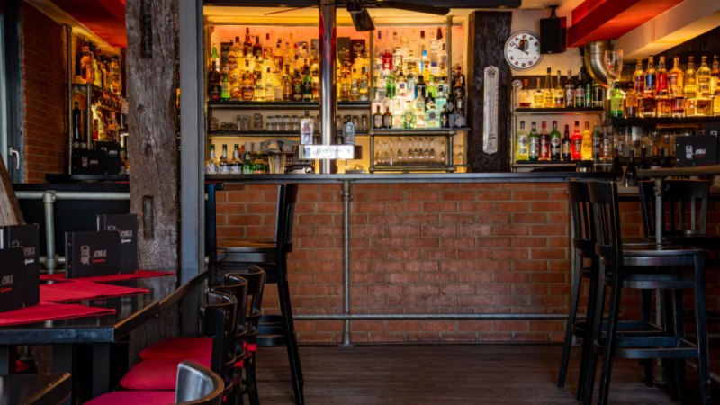 Gemütliche Bar mit Backsteinwand, gut bestücktem Regal und roten Sitzpolstern. Schwarze Tische und Stühle, warme Beleuchtung., © Café Bar Zill Gemütliche Bar mit Backsteinwand, gut bestücktem Regal und roten Sitzpolstern. Schwarze Tische und Stühle, warme Beleuchtung., © Café Bar Zill