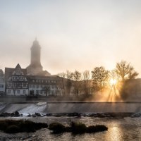 Nebelverhangene Stadtansicht von N&uuml;rtingen mit Fachwerkh&auml;usern und Kirchturm im Morgenlicht. Die Sonne bricht durch die B&auml;ume am Fluss., &copy; Stadt N&uuml;rtingen