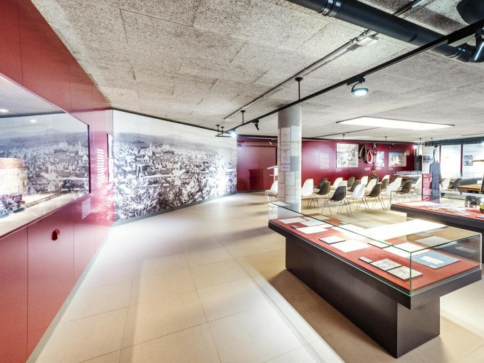 Modernes Museum mit Glasvitrinen, Sitzbereich und großem Wandbild. Helle Beleuchtung und rote Wände schaffen eine einladende Atmosphäre., © Stadt Göppingen Modernes Museum mit Glasvitrinen, Sitzbereich und großem Wandbild. Helle Beleuchtung und rote Wände schaffen eine einladende Atmosphäre., © Stadt Göppingen