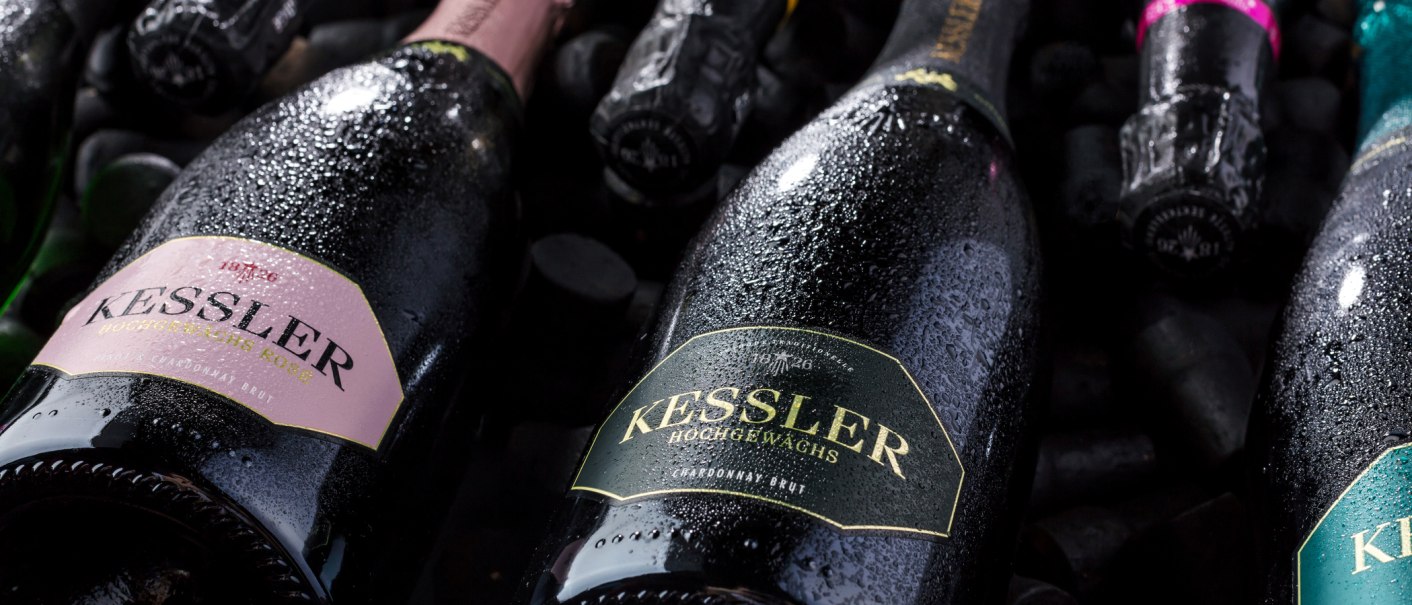 Nahaufnahme von Kessler Sektflaschen, die mit Wassertropfen bedeckt sind. Die Etiketten zeigen verschiedene Sorten wie Rosé und Chardonnay Brut., © none