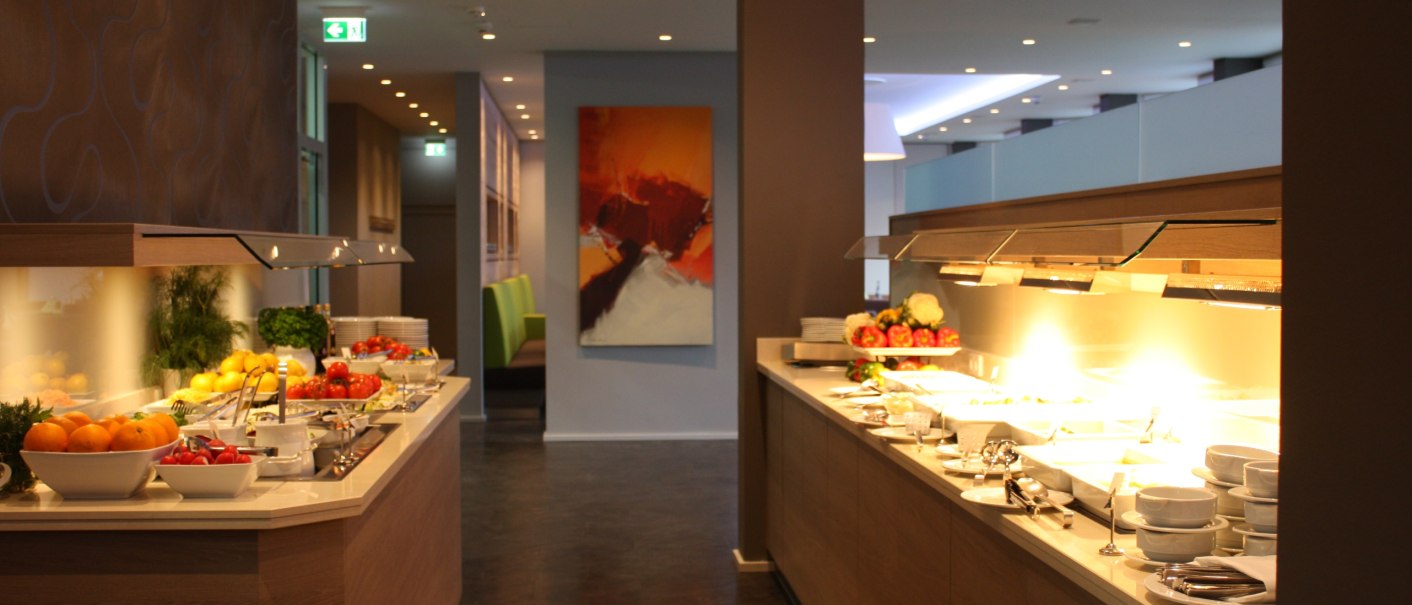 Ein stilvolles Buffet in einem Restaurant mit Obst, Geschirr und warmem Licht. Moderne Einrichtung mit Kunst an der Wand., © Hotel am Schlossberg Herrenberg Ein stilvolles Buffet in einem Restaurant mit Obst, Geschirr und warmem Licht. Moderne Einrichtung mit Kunst an der Wand., © Hotel am Schlossberg Herrenberg