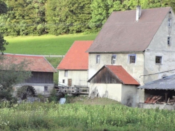 Ein altes Bauernhaus mit roten Ziegeldächern und einem Wasserrad, umgeben von grünen Wiesen und Wäldern., © SwabianTravel Ein altes Bauernhaus mit roten Ziegeldächern und einem Wasserrad, umgeben von grünen Wiesen und Wäldern., © SwabianTravel