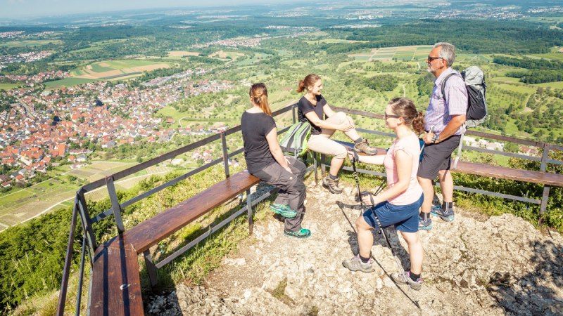 Vier Personen genießen die Aussicht vom Beurener Fels. Im Hintergrund erstreckt sich eine weite Landschaft mit Feldern und Dörfern., © hochgehberge