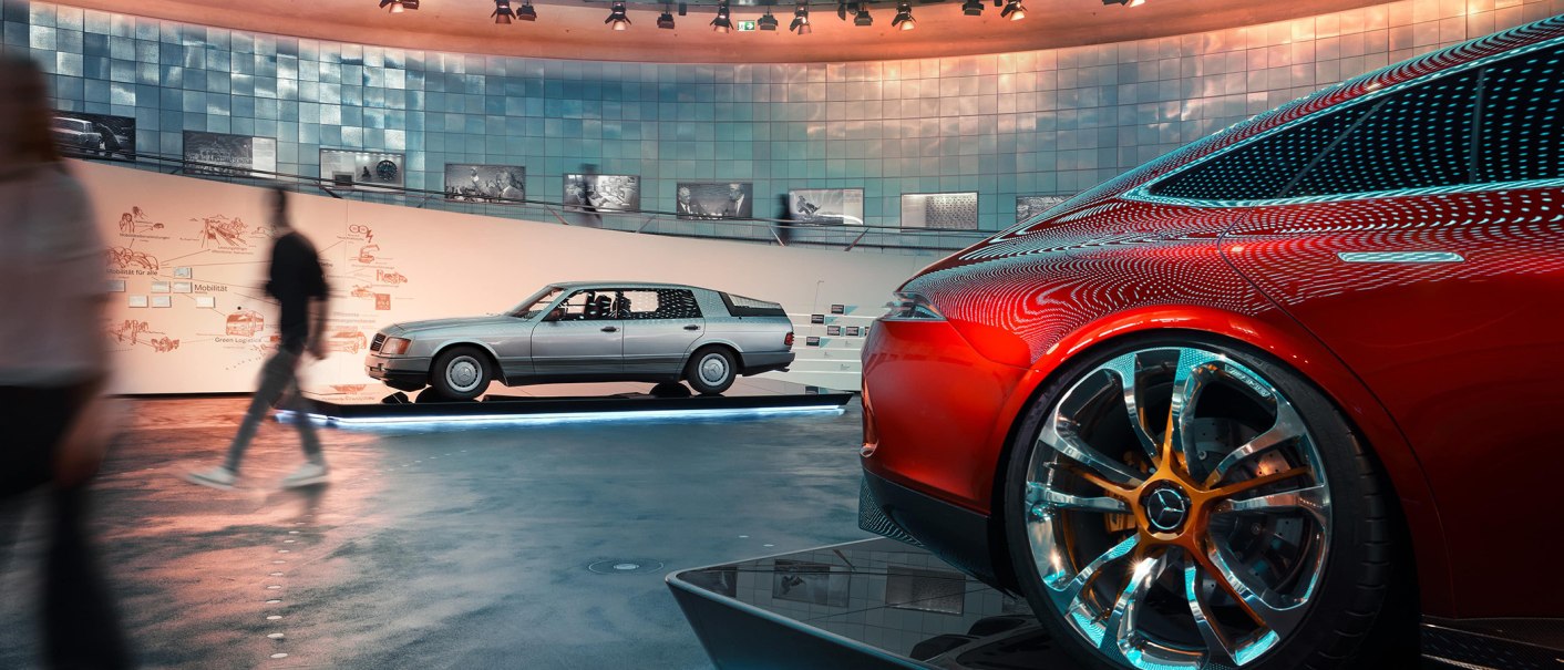Innenansicht des Mercedes-Benz Museums mit einem roten und einem silbernen Auto. Besucher gehen vorbei, moderne Architektur und Beleuchtung im Hintergrund., © Mercedes-Benz Heritage GmbH Innenansicht des Mercedes-Benz Museums mit einem roten und einem silbernen Auto. Besucher gehen vorbei, moderne Architektur und Beleuchtung im Hintergrund., © Mercedes-Benz Heritage GmbH