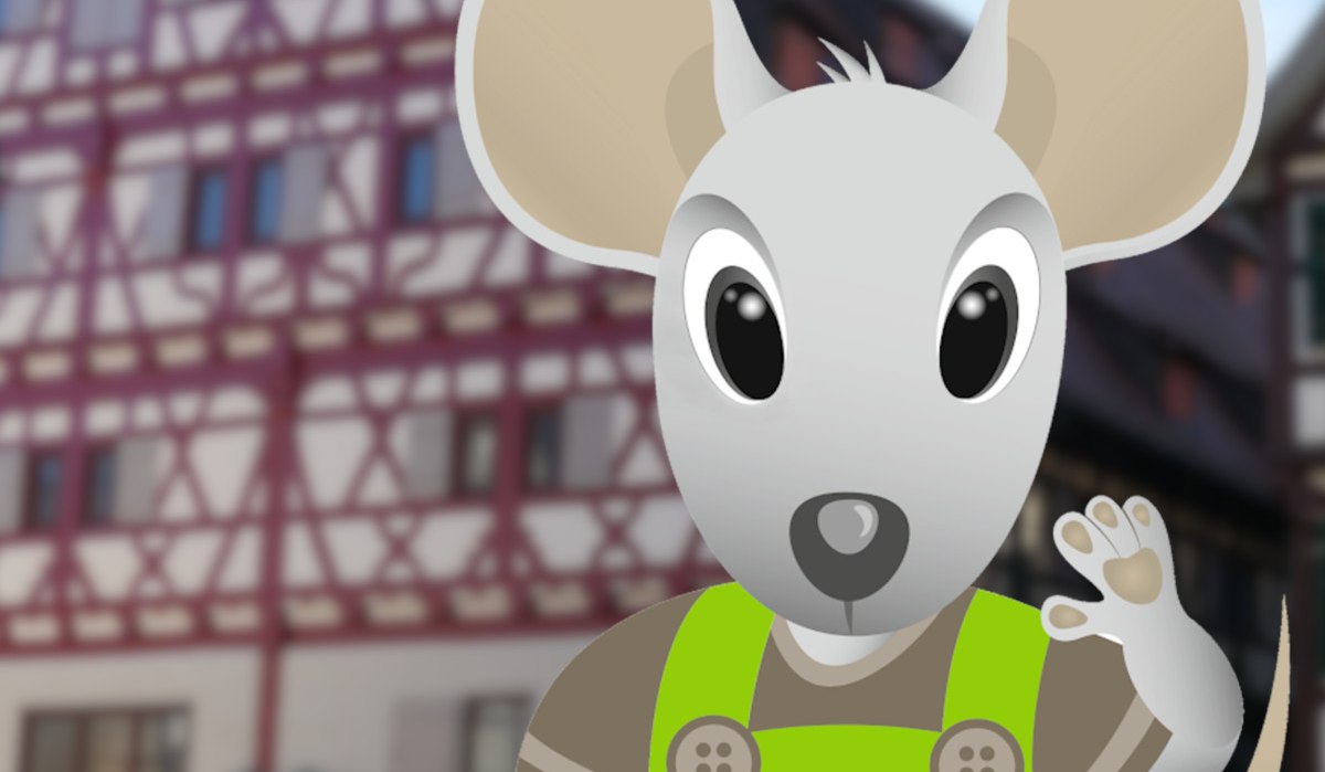 Eine animierte Maus namens Herri in gr&uuml;ner Latzhose steht vor einem Fachwerkgeb&auml;ude. Die Maus winkt freundlich., &copy; Stadt Herrenberg