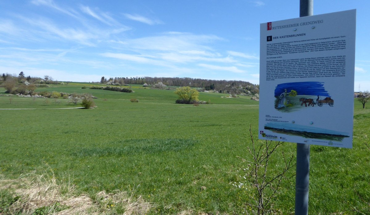 Ein Schild am Rutesheimer Grenzweg informiert über den Kastenbrunnen. Im Hintergrund erstreckt sich eine grüne Landschaft unter einem blauen Himmel., © Natur.Nah. Schönbuch & Heckengäu Ein Schild am Rutesheimer Grenzweg informiert über den Kastenbrunnen. Im Hintergrund erstreckt sich eine grüne Landschaft unter einem blauen Himmel., © Natur.Nah. Schönbuch & Heckengäu