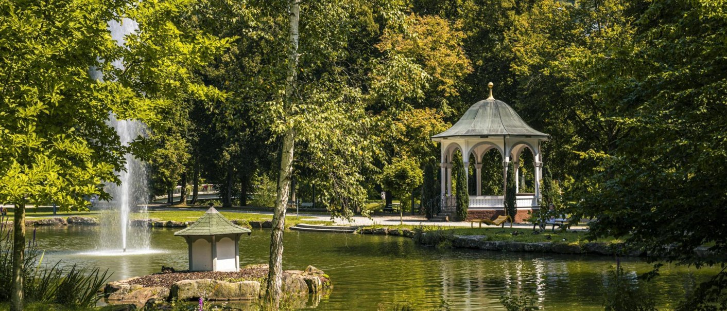Ein idyllischer Park mit einem Pavillon und einem Springbrunnen in einem Teich, umgeben von &uuml;ppigem Gr&uuml;n und B&auml;umen., &copy; SMG, Sarah Schmid