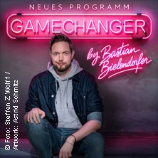 Ein Mann sitzt vor einem leuchtenden Schild mit der Aufschrift 'GameChanger by Bastian Bielendorfer'. Er tr&auml;gt eine Jeansjacke und einen grauen Hoodie., &copy; links im Bild