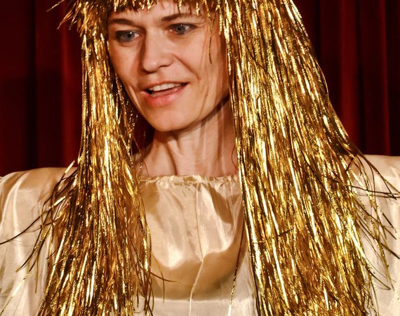 Person mit goldener Per&uuml;cke und Kost&uuml;m steht vor einem roten Vorhang, vermutlich in einem Theaterst&uuml;ck., &copy; Galli Theater Backnang