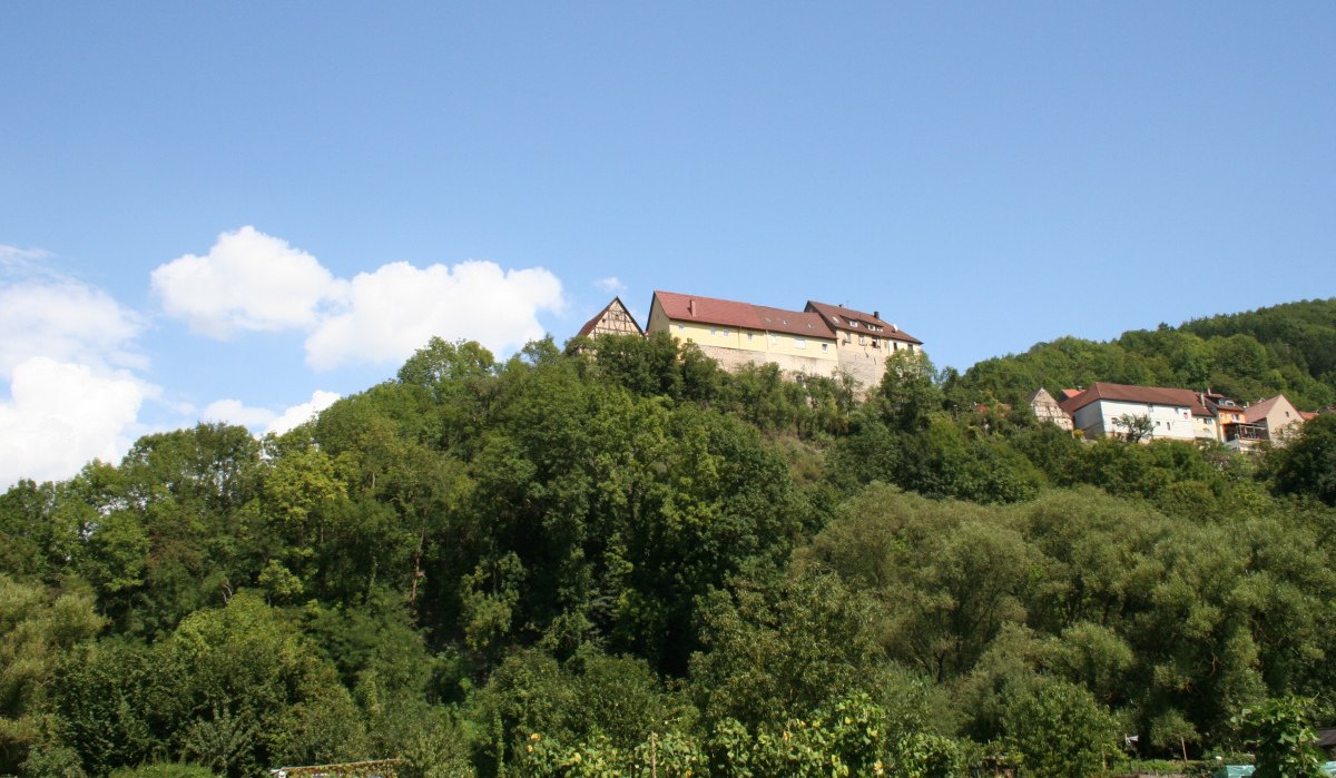 Burg Nagelsberg thront auf einem bewaldeten Hügel unter klarem, blauem Himmel. Im Vordergrund sind Bäume und Sträucher zu sehen., © Touristikgemeinschaft Hohenlohe, Künzelsau / Marion Schlund Burg Nagelsberg thront auf einem bewaldeten Hügel unter klarem, blauem Himmel. Im Vordergrund sind Bäume und Sträucher zu sehen., © Touristikgemeinschaft Hohenlohe, Künzelsau / Marion Schlund