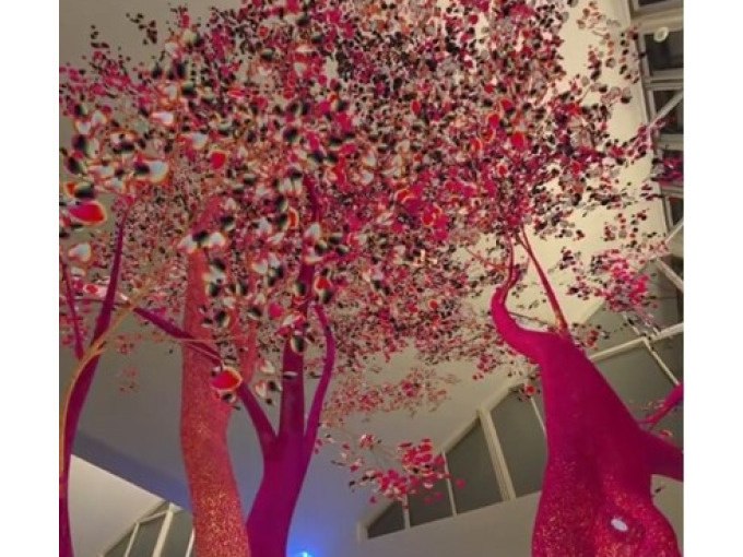 Kunstinstallation mit leuchtend rosa Bäumen und bunten Blättern, die von der Decke eines modernen Innenraums hängen., © Kunsthalle Göppingen Kunstinstallation mit leuchtend rosa Bäumen und bunten Blättern, die von der Decke eines modernen Innenraums hängen., © Kunsthalle Göppingen