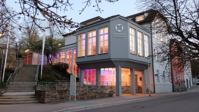 Das Backnanger Bürgerhaus bei Dämmerung, mit beleuchteten Fenstern und kahlen Bäumen im Vordergrund. Eine Treppe führt zum Eingang., © Kultur-und Sportamt Backnang