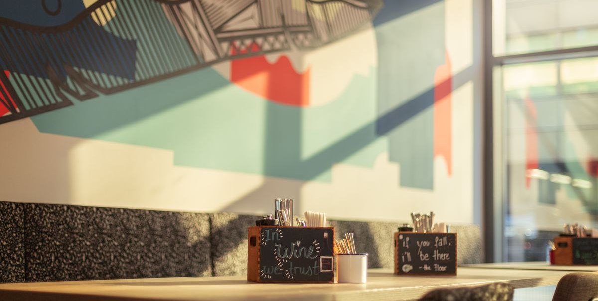Ein Restaurant mit moderner Wandkunst und Tischen, auf denen Besteckbehälter stehen. Sonnenlicht fällt durch die Fenster., © Novum Hospitality Ein Restaurant mit moderner Wandkunst und Tischen, auf denen Besteckbehälter stehen. Sonnenlicht fällt durch die Fenster., © Novum Hospitality