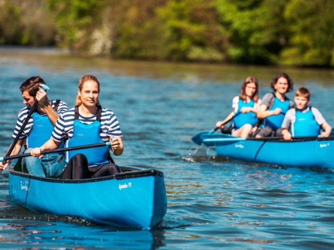 Zwei blaue Kanus mit Menschen paddeln auf einem Fluss. Die Personen tragen gestreifte Shirts und blaue Schwimmwesten. Im Hintergrund ist grüne Vegetation., © Cool-Tours StattReisen Zwei blaue Kanus mit Menschen paddeln auf einem Fluss. Die Personen tragen gestreifte Shirts und blaue Schwimmwesten. Im Hintergrund ist grüne Vegetation., © Cool-Tours StattReisen