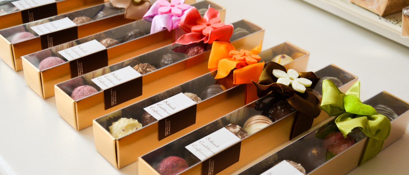 Elegante Pralinenboxen mit bunten Schleifen in einer Reihe angeordnet. Jede Box enth&auml;lt eine Auswahl an Schokoladenpralinen., &copy; Sch&uuml;mli