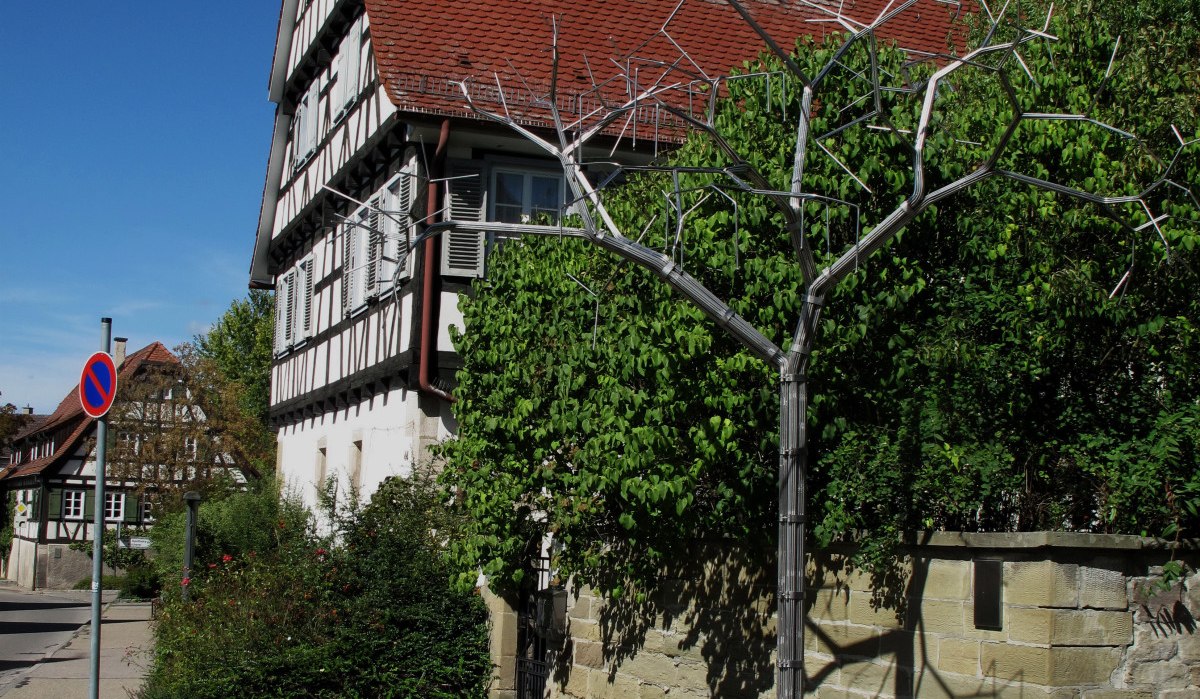 Brunnen mit Metallstruktur vor Fachwerkhaus und blauem Himmel. Historische Architektur und grüne Vegetation im Hintergrund., © RadL Leonberg Brunnen mit Metallstruktur vor Fachwerkhaus und blauem Himmel. Historische Architektur und grüne Vegetation im Hintergrund., © RadL Leonberg