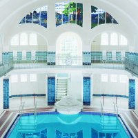 Innenansicht des Merkel'schen Schwimmbads in Esslingen. Das Becken ist von blauen Fliesen umgeben, mit hohen Fenstern und einem kunstvollen Glasfenster., © Esslinger Stadtmarketing & Tourismus GmbH