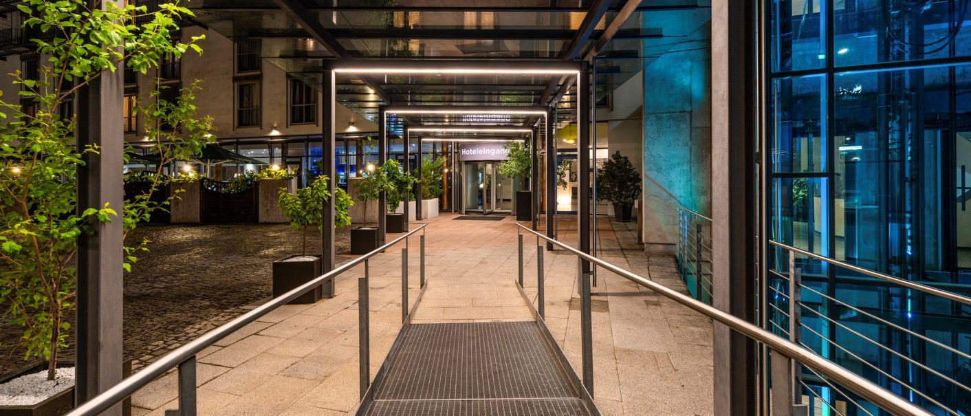 Ein moderner Hoteleingang mit Glasüberdachung, beleuchtetem Weg und Pflanzen in Töpfen. Der Eingang wirkt einladend und stilvoll., © Plaza Residence Stuttgart-Ditzingen Ein moderner Hoteleingang mit Glasüberdachung, beleuchtetem Weg und Pflanzen in Töpfen. Der Eingang wirkt einladend und stilvoll., © Plaza Residence Stuttgart-Ditzingen