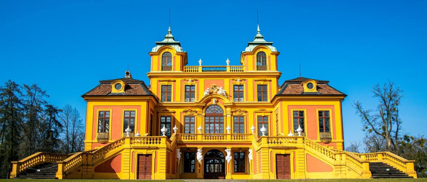 Das Schloss Favorite in Ludwigsburg strahlt in leuchtendem Gelb und Orange unter einem klaren blauen Himmel. Die Architektur ist barock., © Stuttgart-Marketing GmbH, Sarah Schmid