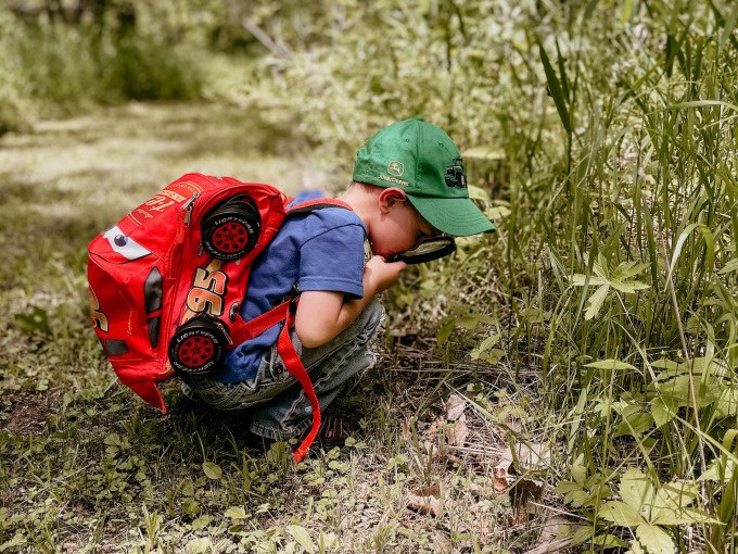 Ein Kind mit rotem Rucksack und gr&uuml;ner Kappe erkundet mit einer Lupe die Pflanzenwelt auf einer Wiese., &copy; Stadt N&uuml;rtingen