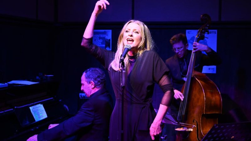 Eine S&auml;ngerin mit Mikrofon, begleitet von einem Pianisten und einem Kontrabassisten, performt auf einer B&uuml;hne in stimmungsvoller Beleuchtung., &copy; Foto Heinrich Hofmann