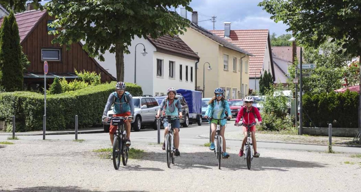 Vier Personen fahren mit Fahrrädern durch eine ruhige Wohngegend. Sie tragen Helme und sind sportlich gekleidet. Im Hintergrund sind Häuser und Autos zu sehen., © Schwäbische Alb Tourismusverband e.V. Vier Personen fahren mit Fahrrädern durch eine ruhige Wohngegend. Sie tragen Helme und sind sportlich gekleidet. Im Hintergrund sind Häuser und Autos zu sehen., © Schwäbische Alb Tourismusverband e.V.
