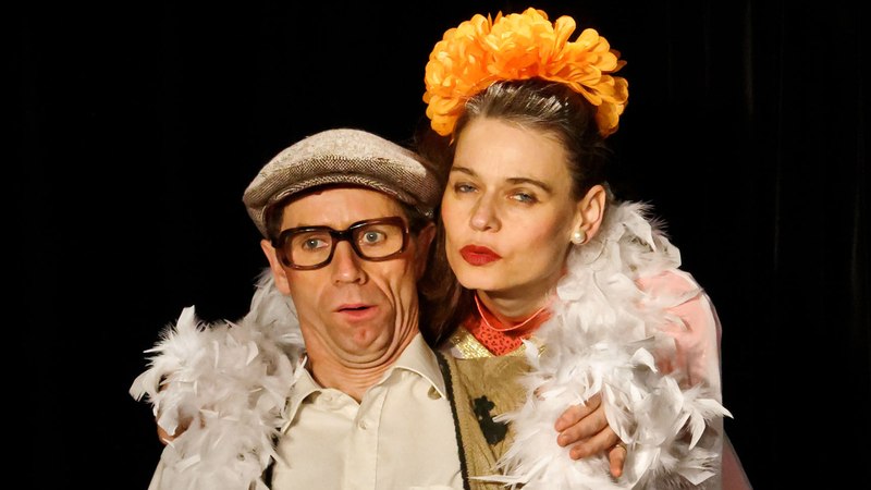 Ein Mann mit Brille und M&uuml;tze posiert neben einer Frau mit Blumen im Haar und Federboa. Beide haben am&uuml;sierte Gesichtsausdr&uuml;cke., &copy; Galli Theater Backnang