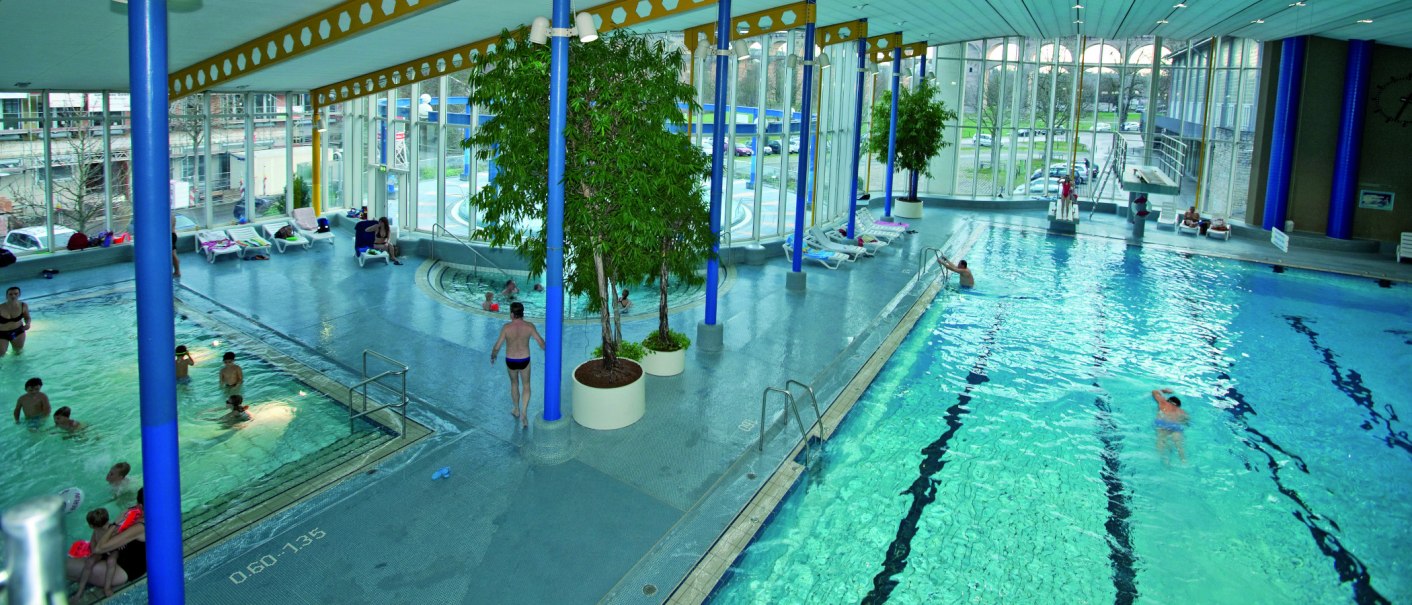 Ein Hallenbad mit mehreren Schwimmbecken, Liegestühlen und großen Fenstern. Menschen schwimmen und entspannen. Pflanzen dekorieren den Raum., © Stuttgart-Marketing GmbH Ein Hallenbad mit mehreren Schwimmbecken, Liegestühlen und großen Fenstern. Menschen schwimmen und entspannen. Pflanzen dekorieren den Raum., © Stuttgart-Marketing GmbH