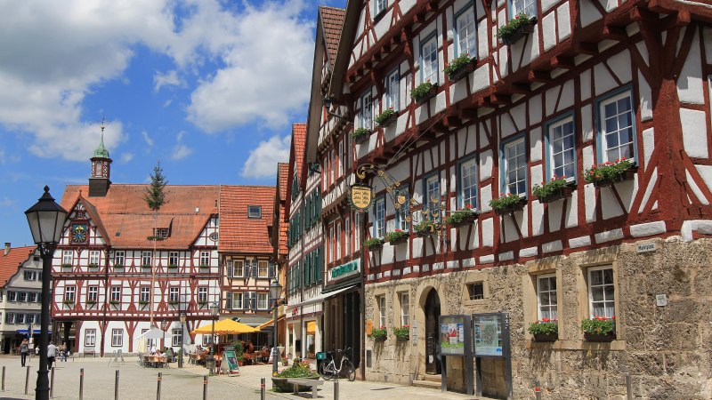 Fachwerkhäuser am Marktplatz von Bad Urach, blauer Himmel mit Wolken, Menschen sitzen draußen, Blumen schmücken die Fenster., © Armin Dieter Fachwerkhäuser am Marktplatz von Bad Urach, blauer Himmel mit Wolken, Menschen sitzen draußen, Blumen schmücken die Fenster., © Armin Dieter
