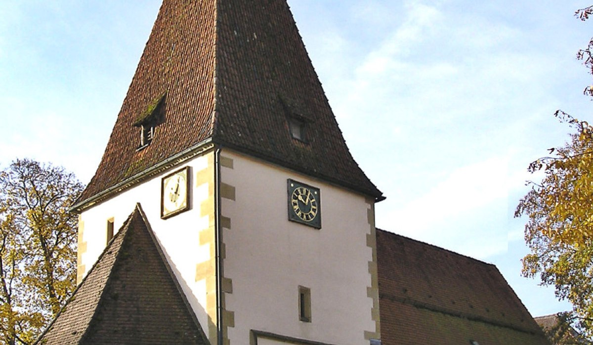 Die Afra Kirche in Täferrot mit spitzem Turm, Uhr und weißen Wänden, umgeben von Bäumen und blauem Himmel., © Gemeindeverwaltung Täferrot Die Afra Kirche in Täferrot mit spitzem Turm, Uhr und weißen Wänden, umgeben von Bäumen und blauem Himmel., © Gemeindeverwaltung Täferrot