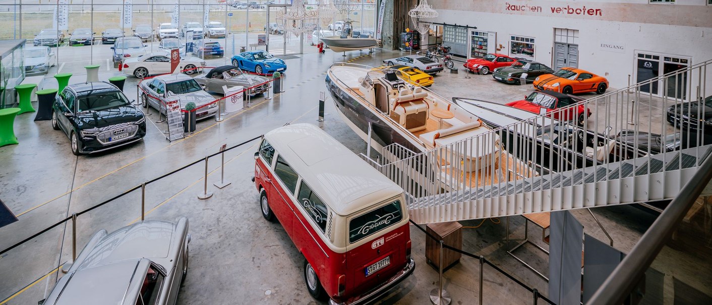 Ausstellungshalle mit verschiedenen Autos, Booten und Motorrädern. Im Vordergrund ein roter VW-Bus, im Hintergrund diverse Fahrzeuge und Boote., © V8 HOTEL Ausstellungshalle mit verschiedenen Autos, Booten und Motorrädern. Im Vordergrund ein roter VW-Bus, im Hintergrund diverse Fahrzeuge und Boote., © V8 HOTEL