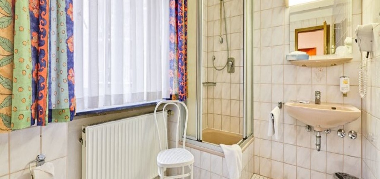 Ein helles Badezimmer mit Dusche, Waschbecken, Stuhl und bunten Vorhängen. Fliesen an Wänden und Boden, Handtücher und ein Föhn sind vorhanden., © ARNOTEL GmbH Ein helles Badezimmer mit Dusche, Waschbecken, Stuhl und bunten Vorhängen. Fliesen an Wänden und Boden, Handtücher und ein Föhn sind vorhanden., © ARNOTEL GmbH