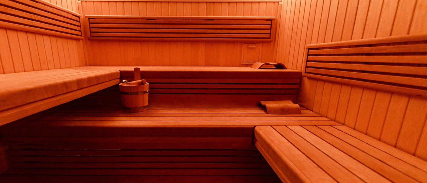 Eine leere Sauna mit Holzbänken und einem Eimer. Die Wände und Bänke sind aus hellem Holz gefertigt., © Plaza Residence Stuttgart-Ditzingen Eine leere Sauna mit Holzbänken und einem Eimer. Die Wände und Bänke sind aus hellem Holz gefertigt., © Plaza Residence Stuttgart-Ditzingen