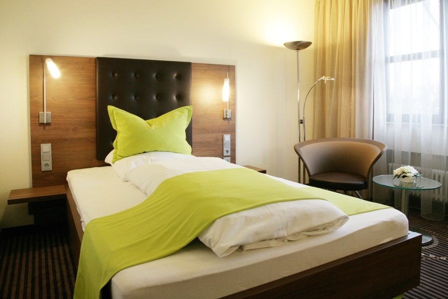 Ein modernes Einzelzimmer mit einem Bett, grünem Überwurf, Sessel und Glastisch vor einem Fenster mit Vorhängen., © Hotel Fuchsen Ein modernes Einzelzimmer mit einem Bett, grünem Überwurf, Sessel und Glastisch vor einem Fenster mit Vorhängen., © Hotel Fuchsen