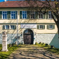 Das Schlossmuseum in Kirchheim unter Teck zeigt ein historisches Geb&auml;ude mit gr&uuml;nen Fensterl&auml;den und Gedenksteinen im Vordergrund, umgeben von einem gepflegten Garten., &copy; Stuttgart-Marketing GmbH, Sarah Schmid